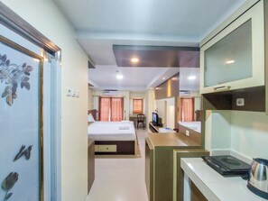 A hotel room with a bed, a desk, a chair, a television, and a coffee maker. - Good Deal And Homey Studio Apartment At Mansyur Residence (Medan)