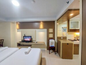 A hotel room with a bed, a desk with a computer, a TV, and a mirror. - Good Deal And Homey Studio Apartment At Mansyur Residence (Medan)