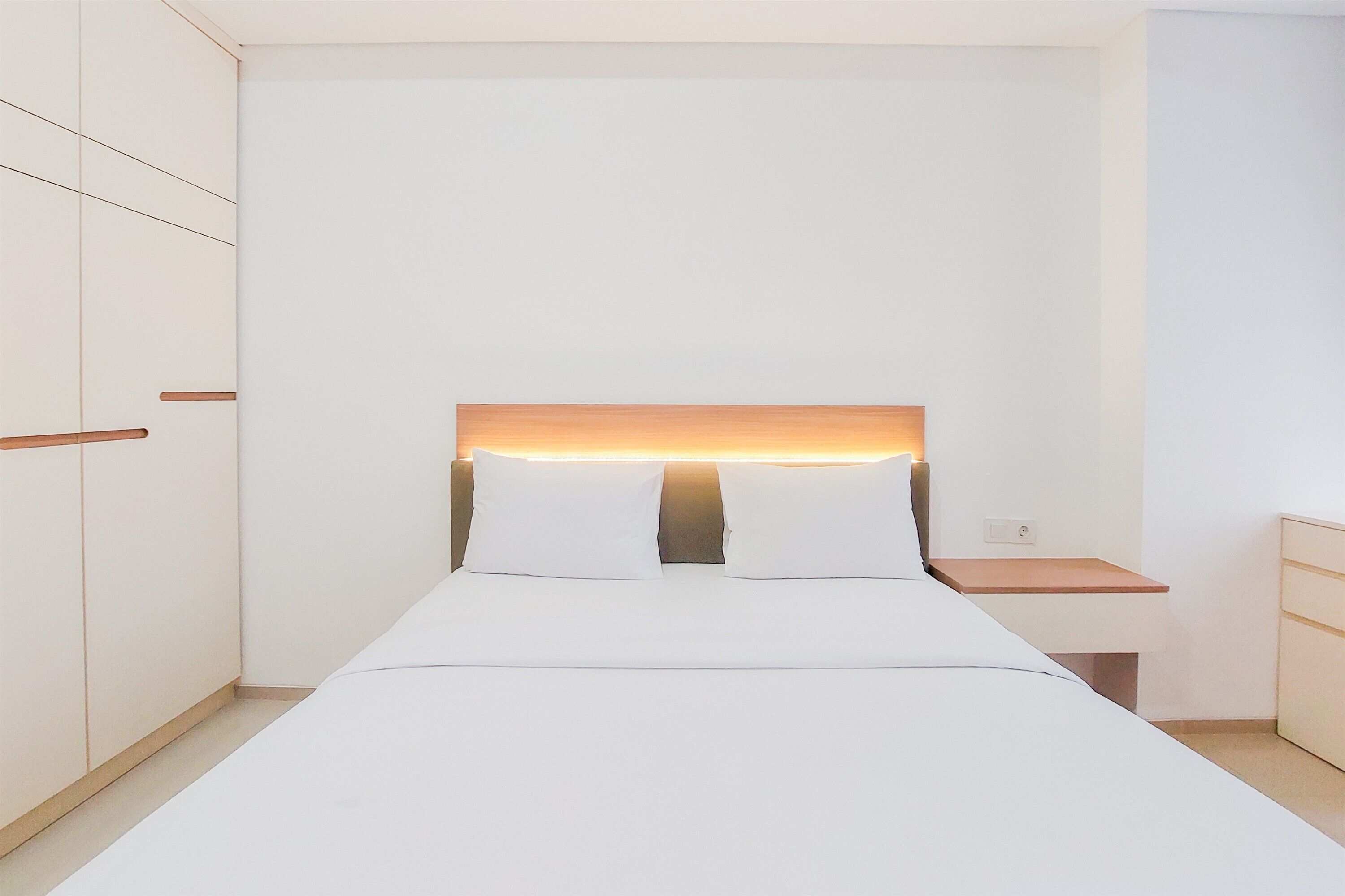 Une chambre à coucher au style minimaliste, avec un lit, des tables de chevet et des armoires encastrées.