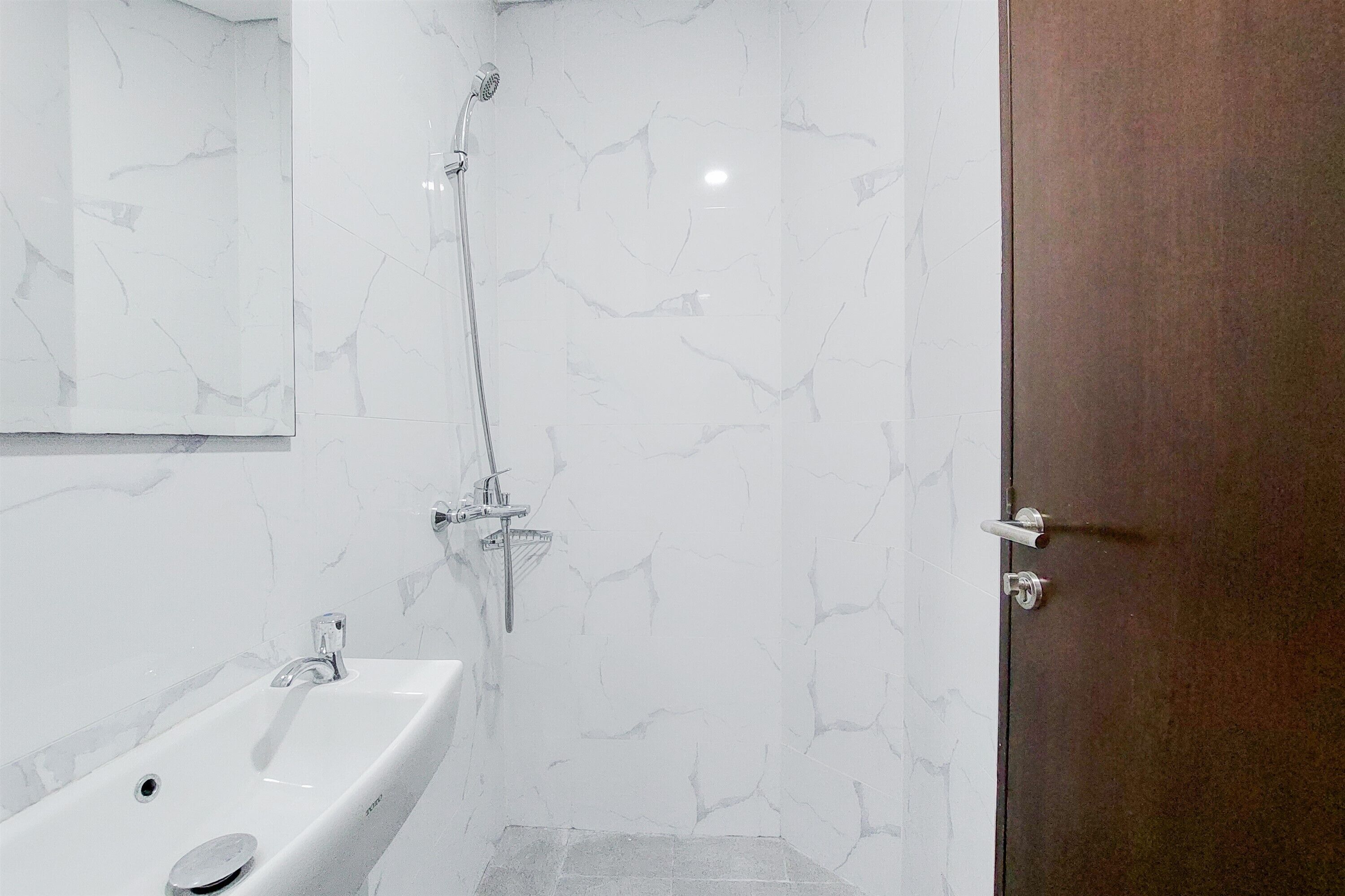 A bathroom with a white marble sink, a shower with a handheld showerhead, and a wooden door.