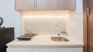 A kitchen with a white countertop, a stainless steel sink, and wooden cabinets. - Cozy Living And Nice Studio At Pacific Garden Alam Sutera Apartment (Tangerang)