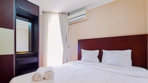 A hotel room with a neatly made bed, a large mirror, and an air conditioning unit on the wall. - Homey And Comfy Stay 2Br Mangga Dua Apartment (Jakarta)