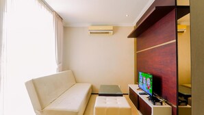 A modern living room with a sofa, a small table, a TV, and a built-in entertainment unit. - Homey And Comfy Stay 2Br Mangga Dua Apartment (Jakarta)