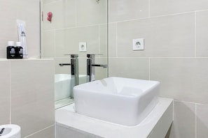 A modern bathroom with a white bathtub, a glass shower enclosure, and a toilet. There are toiletries on the wall. - Good And Cozy Stay Studio Daan Mogot City Apartment (Jakarta)