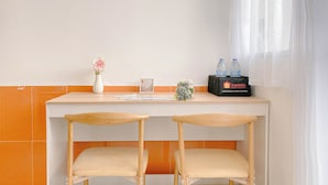 Ein kleiner Hotel-Empfangsbereich mit einer weißen Theke, zwei Holzstühlen, einer Vase mit einer Blume, einem gerahmten Bild und einer Auswahl an kleinen Snacks und Getränken.