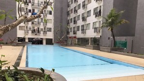 A swimming pool surrounded by a building with balconies and a garden area with plants. - Stylish And Spacious Studio At Apartment Jarrdin Cihampelas (Bandung)
