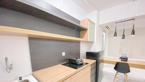 A modern kitchen with a wooden countertop, a sink, and a black refrigerator. There is a small table with a chair and a window with blinds in the background. - Stylish And Spacious Studio At Apartment Jarrdin Cihampelas (Bandung)