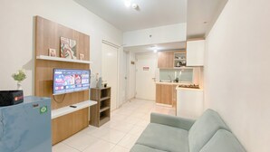 Un salon moderne avec un téléviseur à écran plat, des étagères en bois, un réfrigérateur bleu et un canapé gris clair.