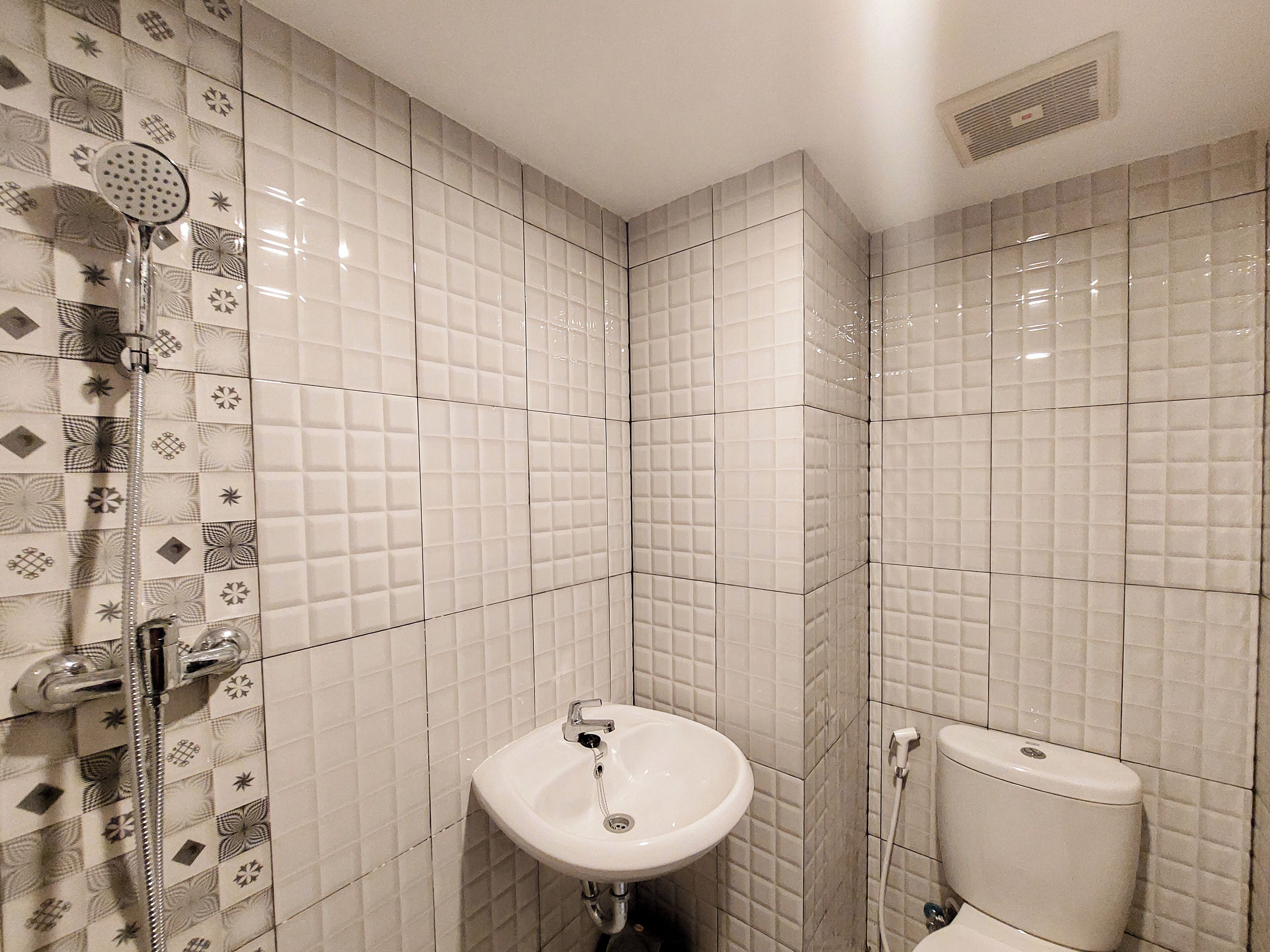 A bathroom with a white sink, toilet, and shower. The walls are tiled with a geometric pattern.
