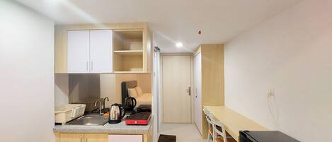 Een compacte keuken met een spoelbak, aanrecht en kasten. Er staat een eettafel met stoelen en een zwarte koelkast.