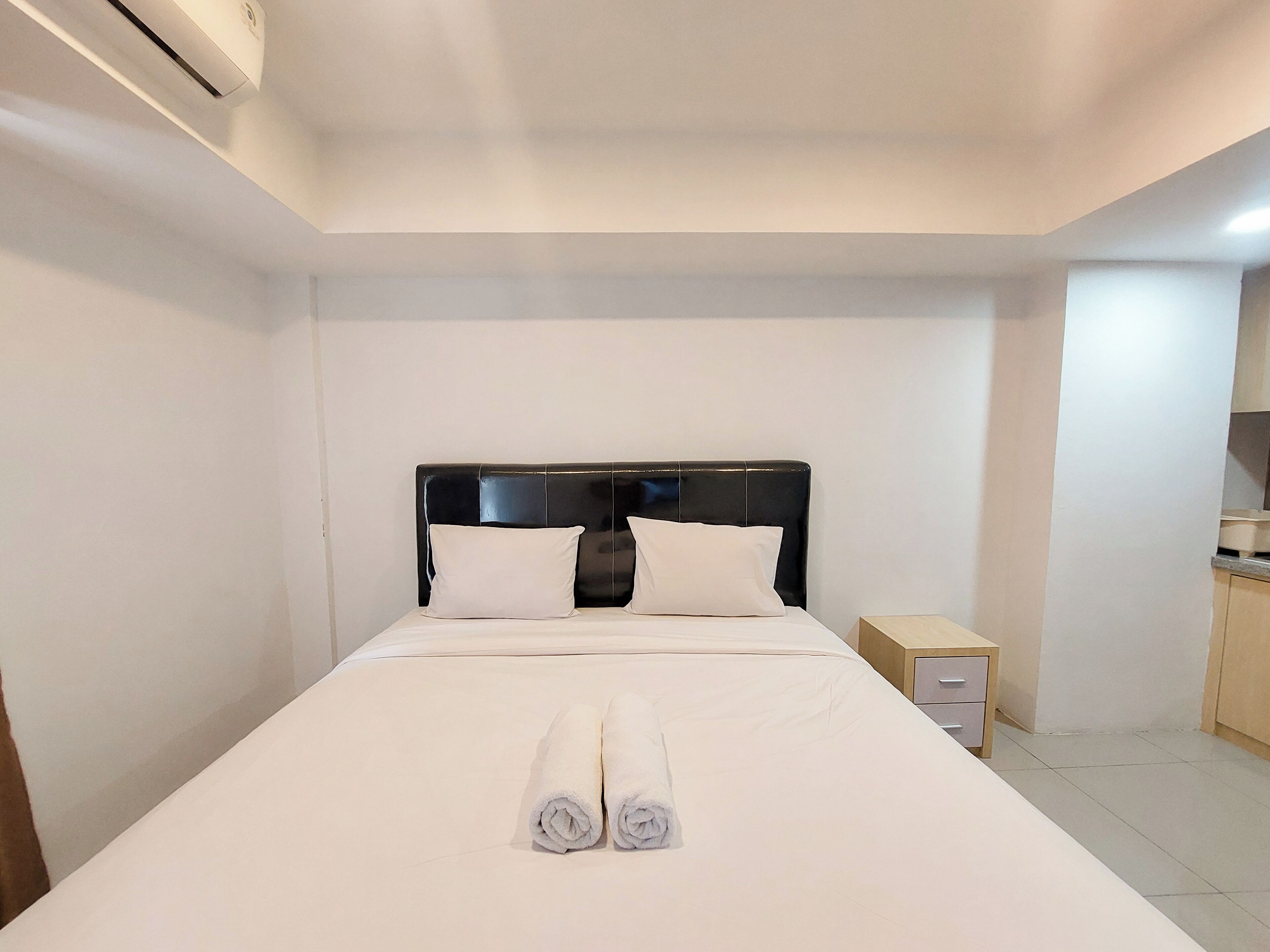 A hotel room with a bed, two pillows, a nightstand, and a small table.