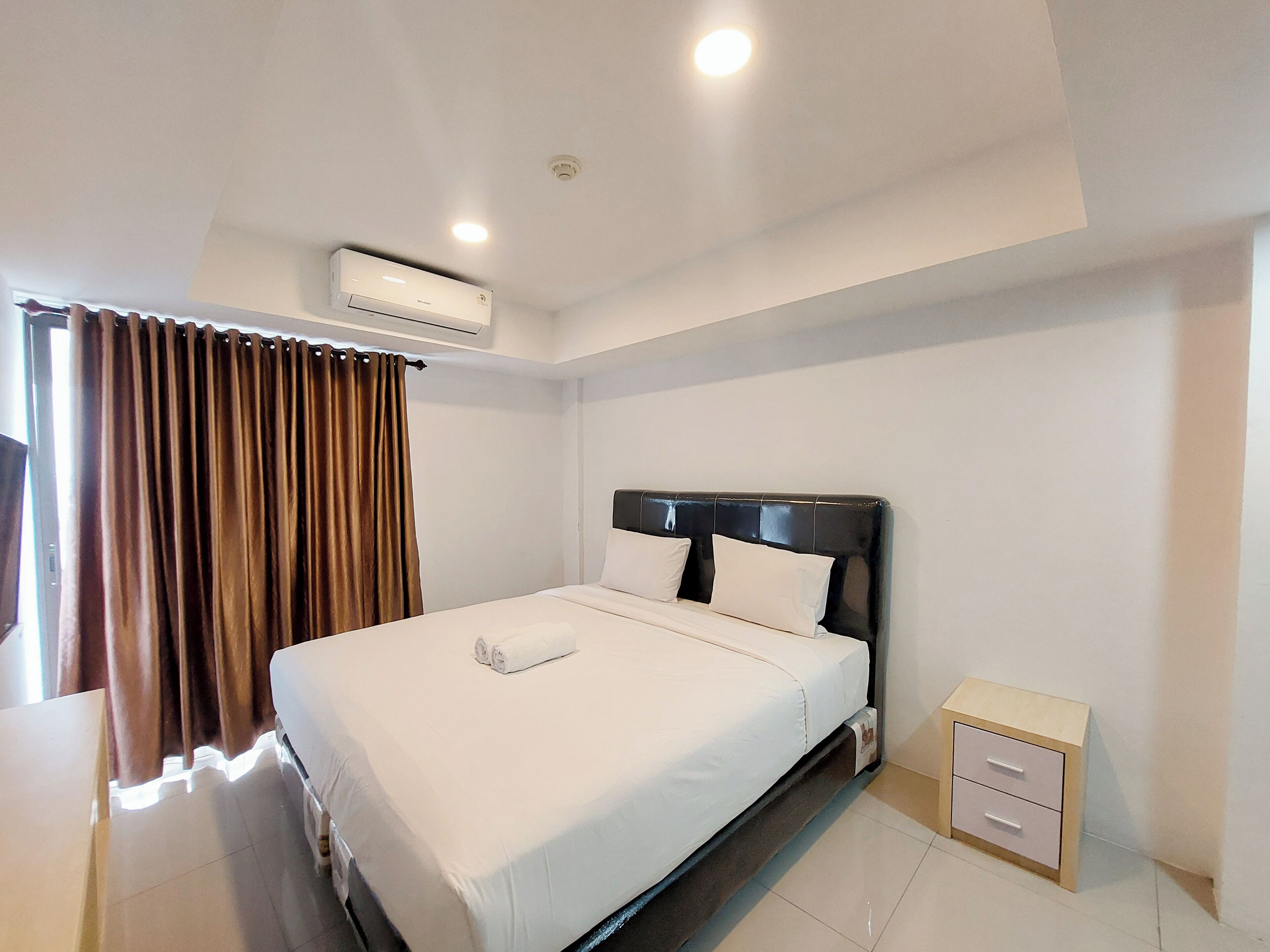 A hotel room with a bed, a nightstand, an air conditioning unit, and a window with curtains.