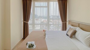 A hotel room with a large bed, beige curtains, a view of the city, and a vase with flowers on the bed. - Comfort And Modern Look 2Br At Menteng Park Apartment (Jakarta)