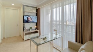 A modern living room with a glass coffee table, a sofa, a TV on a stand, and a large window with curtains. - Comfort And Modern Look 2Br At Menteng Park Apartment (Jakarta)