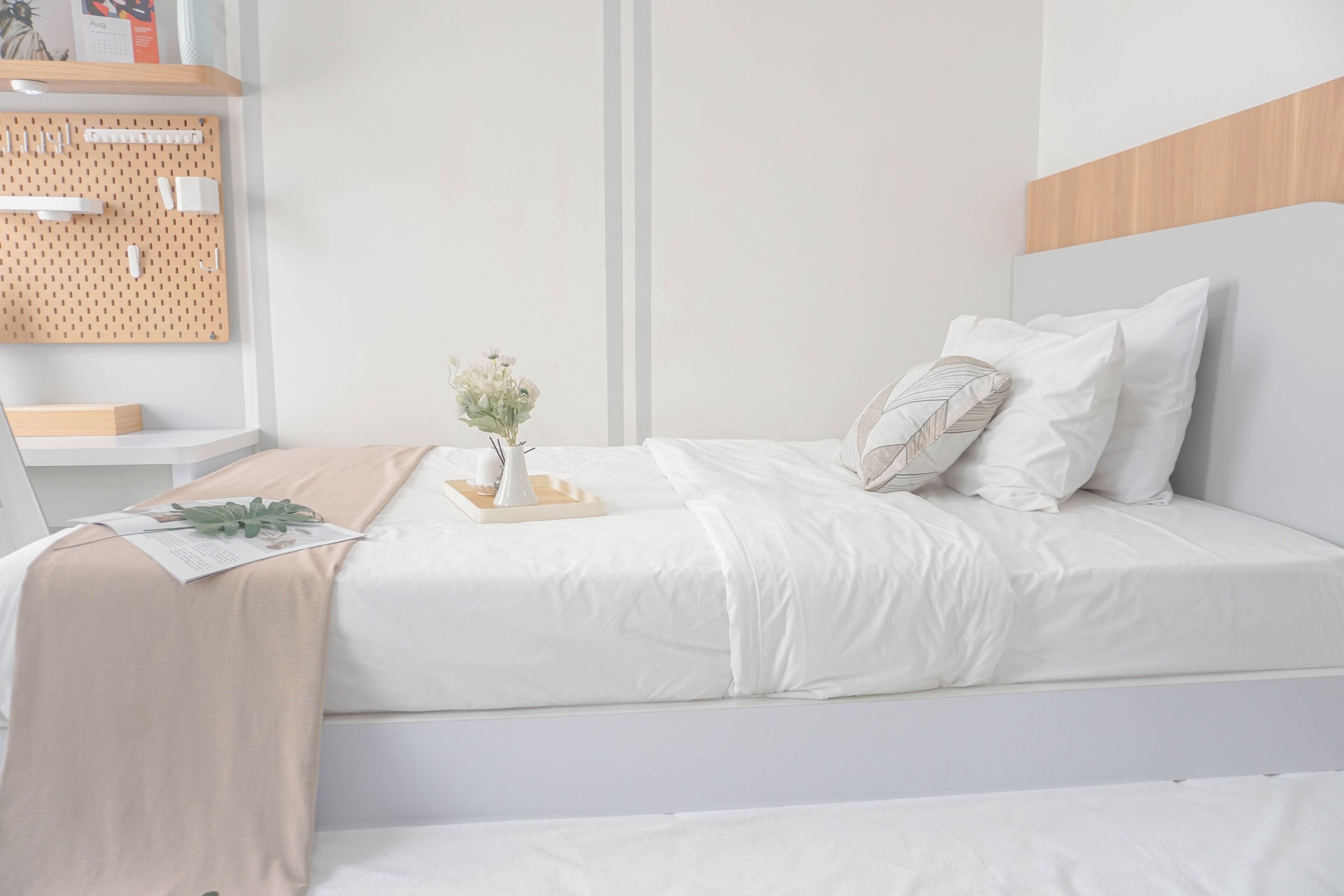 A neatly arranged bedroom with a bed, bedside table, and a wall-mounted pegboard with hooks.