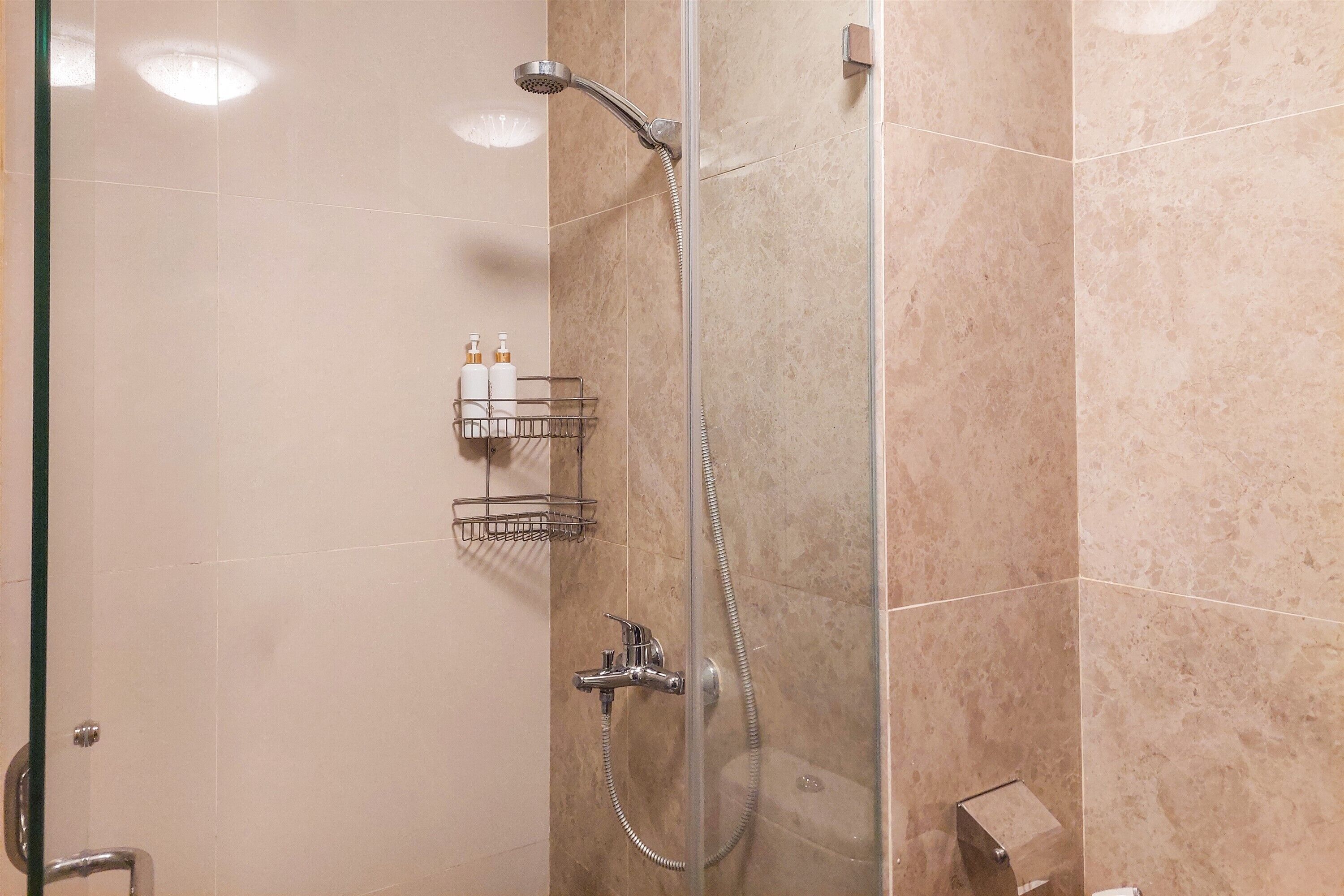 A glass-enclosed shower with a handheld showerhead and a wall-mounted faucet.