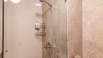 A glass-enclosed shower with a handheld showerhead and a wall-mounted faucet.