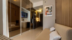 A modern living room with a sofa, a TV, and a kitchen area visible through a glass partition. - Best Combined 2Br At Transpark Bintaro Apartment (South Tangerang)