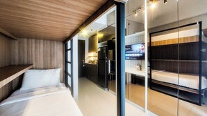 A modern hotel room with a bed, a small kitchenette, and a glass partition separating the sleeping area from the bathroom. - Best Combined 2Br At Transpark Bintaro Apartment (South Tangerang)