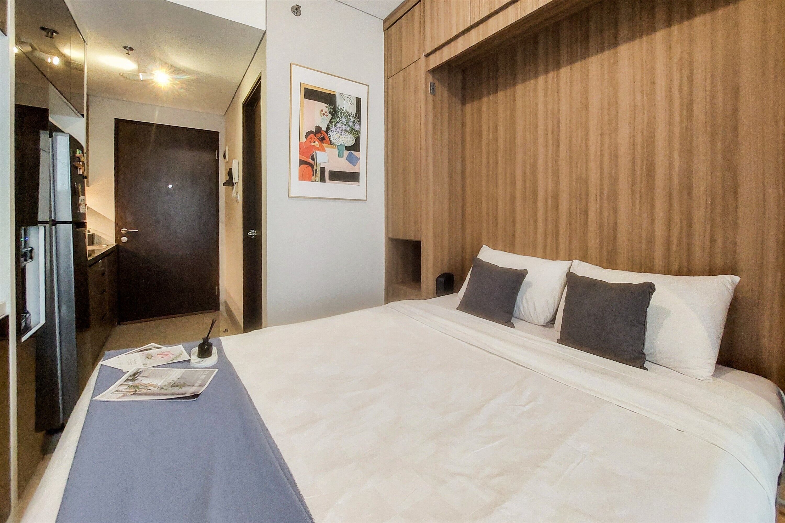 A hotel room with a large bed, a wooden headboard, a framed picture on the wall, and a desk with a lamp.