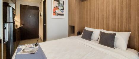A hotel room with a large bed, a wooden headboard, a framed picture on the wall, and a desk with a lamp.