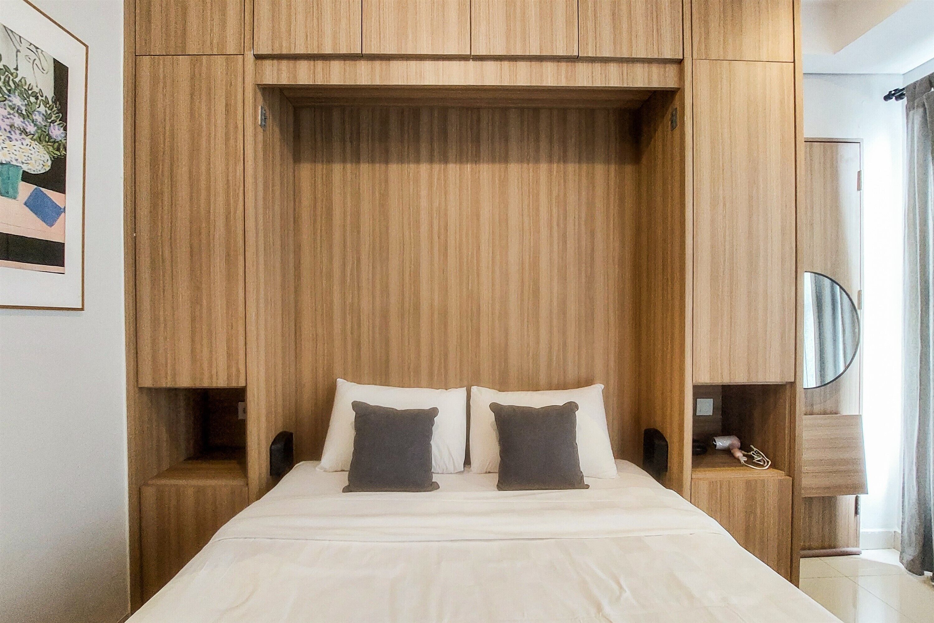 A bedroom with a bed, two pillows, a nightstand, a mirror, and a wooden wardrobe.