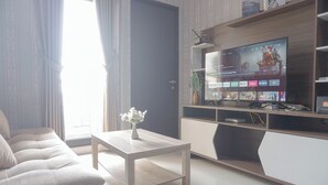 A modern living room with a sofa, a coffee table, and a TV on a wooden stand. - Homey And Best Deal 2Br Transpark Cibubur Apartment (Depok)