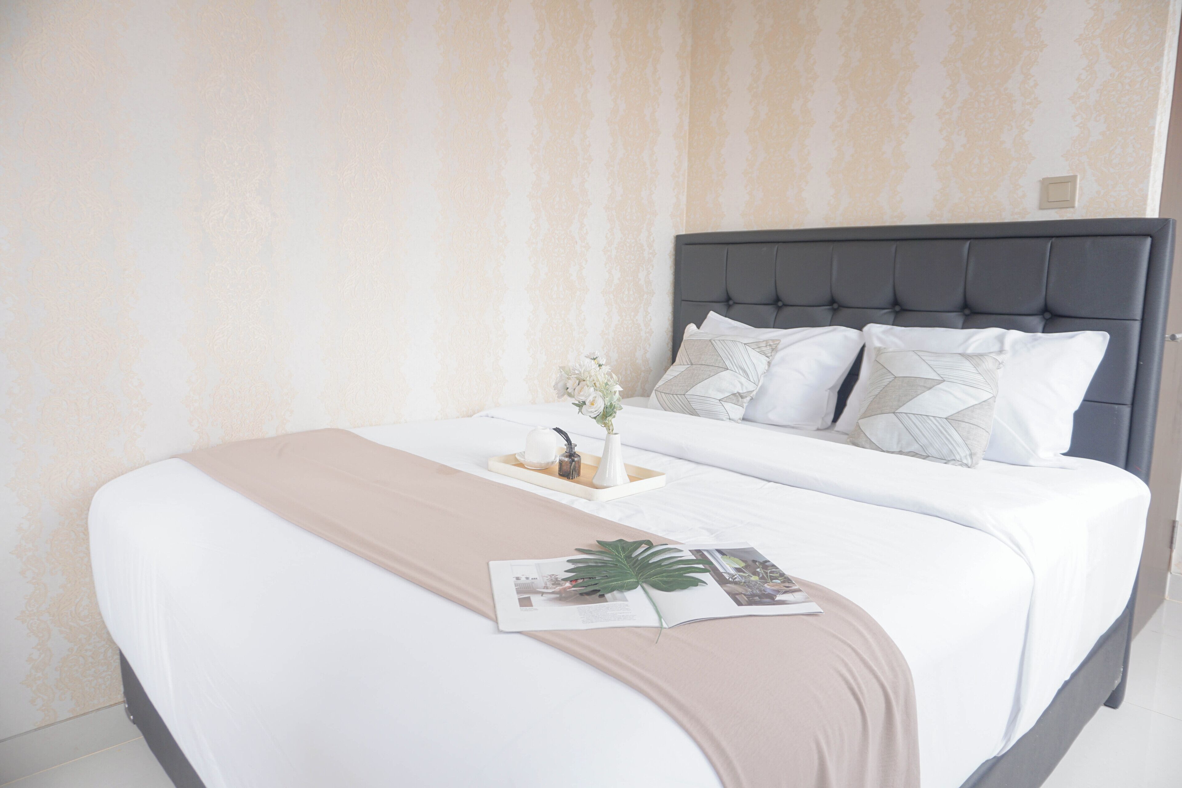 A neatly made bed with a beige bedspread, a white pillow, and a decorative vase with flowers.