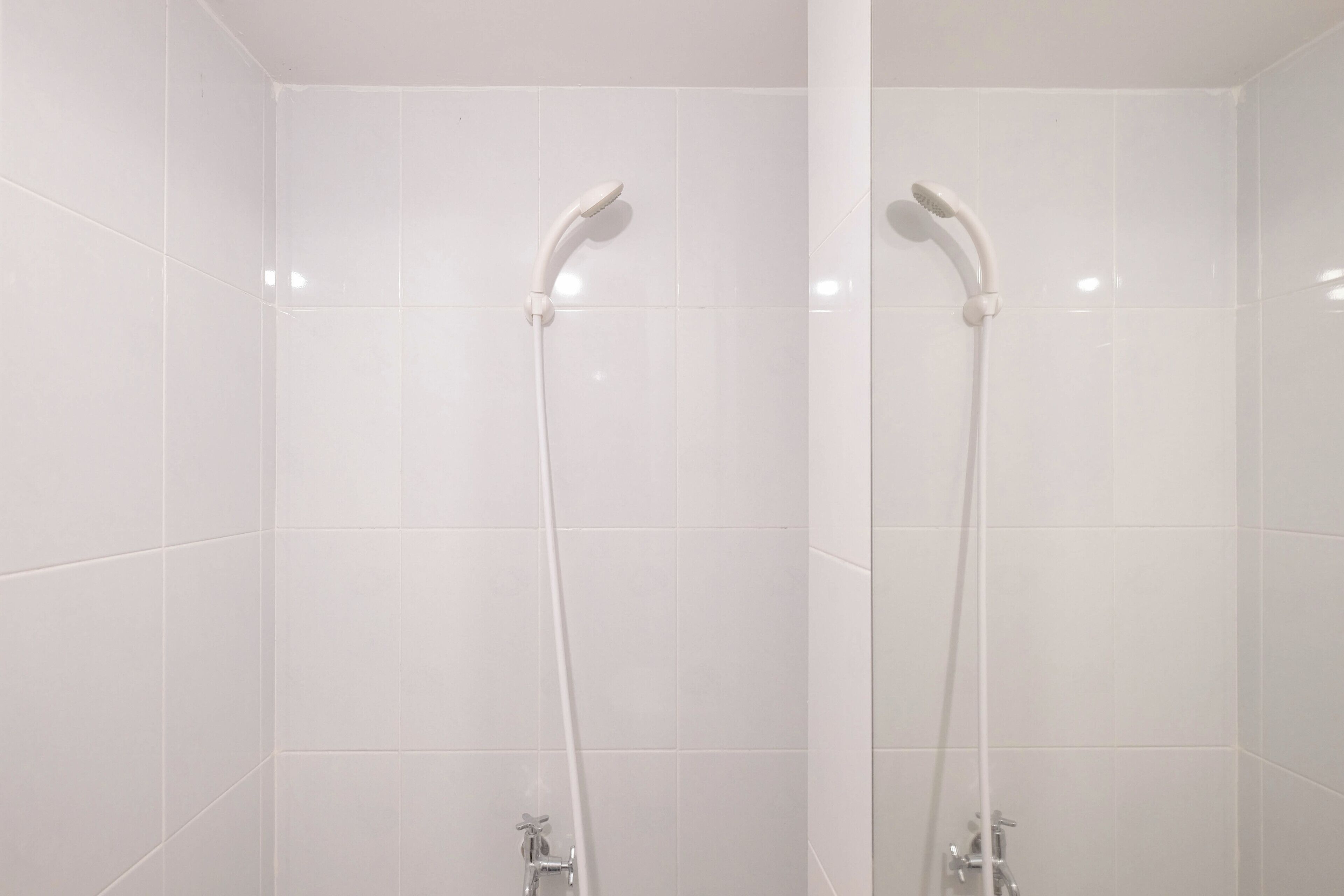 Un baño con paredes de azulejos blancos y una ducha con cabezal de ducha manual.
