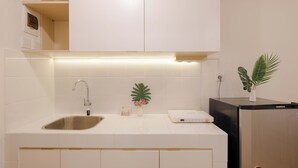 Une cuisine moderne avec des meubles blancs, un évier en acier inoxydable, un plan de travail blanc, une petite plante et un réfrigérateur noir.