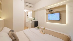 Une chambre d’hôtel moderne avec un grand lit, un téléviseur fixé au mur et une petite kitchenette à l’arrière-plan.