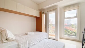 A modern bedroom with a large bed, a wardrobe, and a balcony with a city view. - The Modern Studio Apartment At Parahyangan Residence (Bandung)