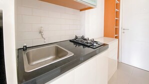 A kitchen with a sink, stove, and white cabinets. - The Modern Studio Apartment At Parahyangan Residence (Bandung)