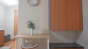 Ein kleiner, moderner Raum mit einem Holzschrank, einer Wanduhr, einem kleinen Tisch mit Topfpflanze und einem runden Sessel.