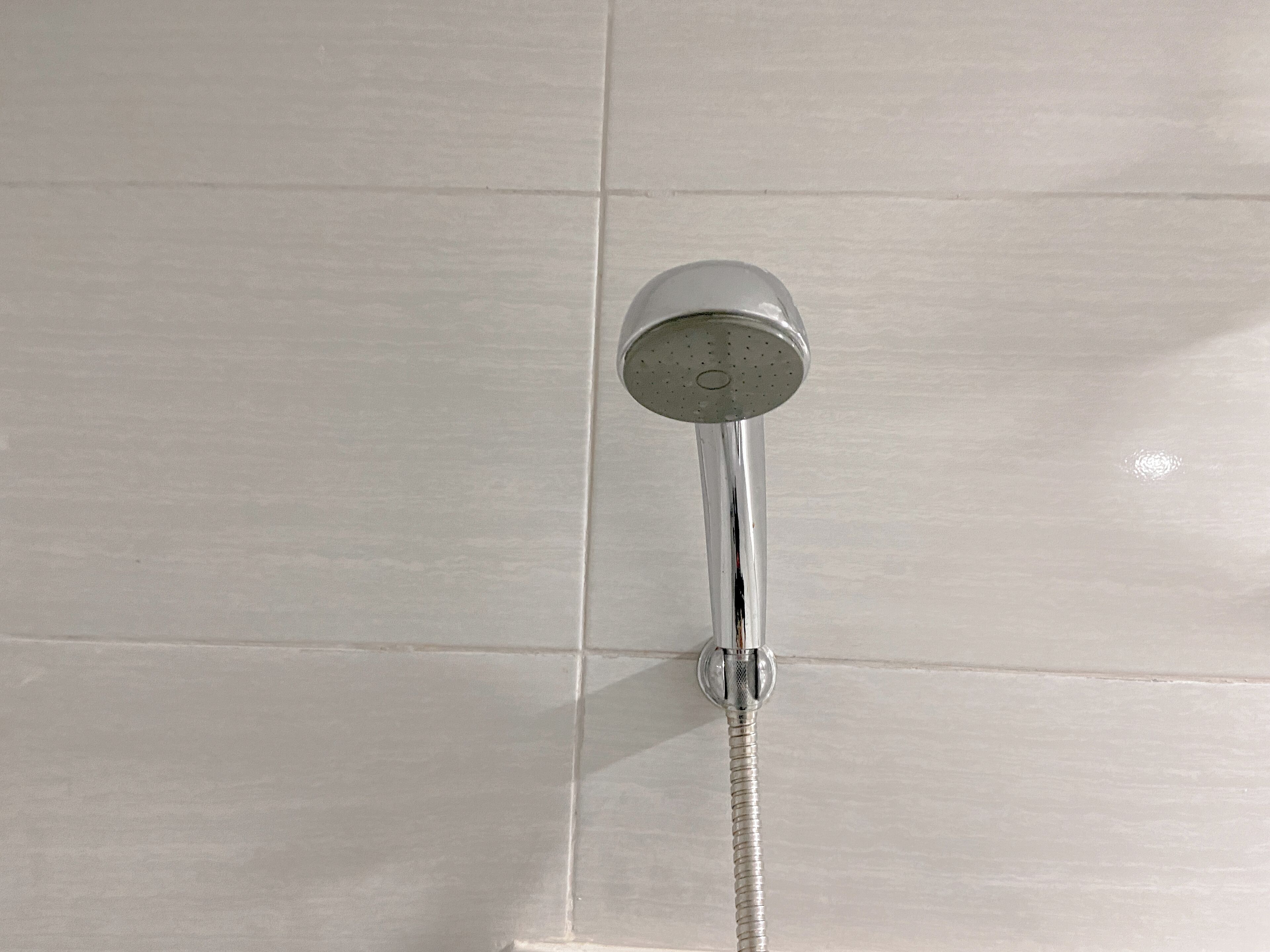 Ein Duschkopf mit flexiblem Schlauch an einer gefliesten Wand.
