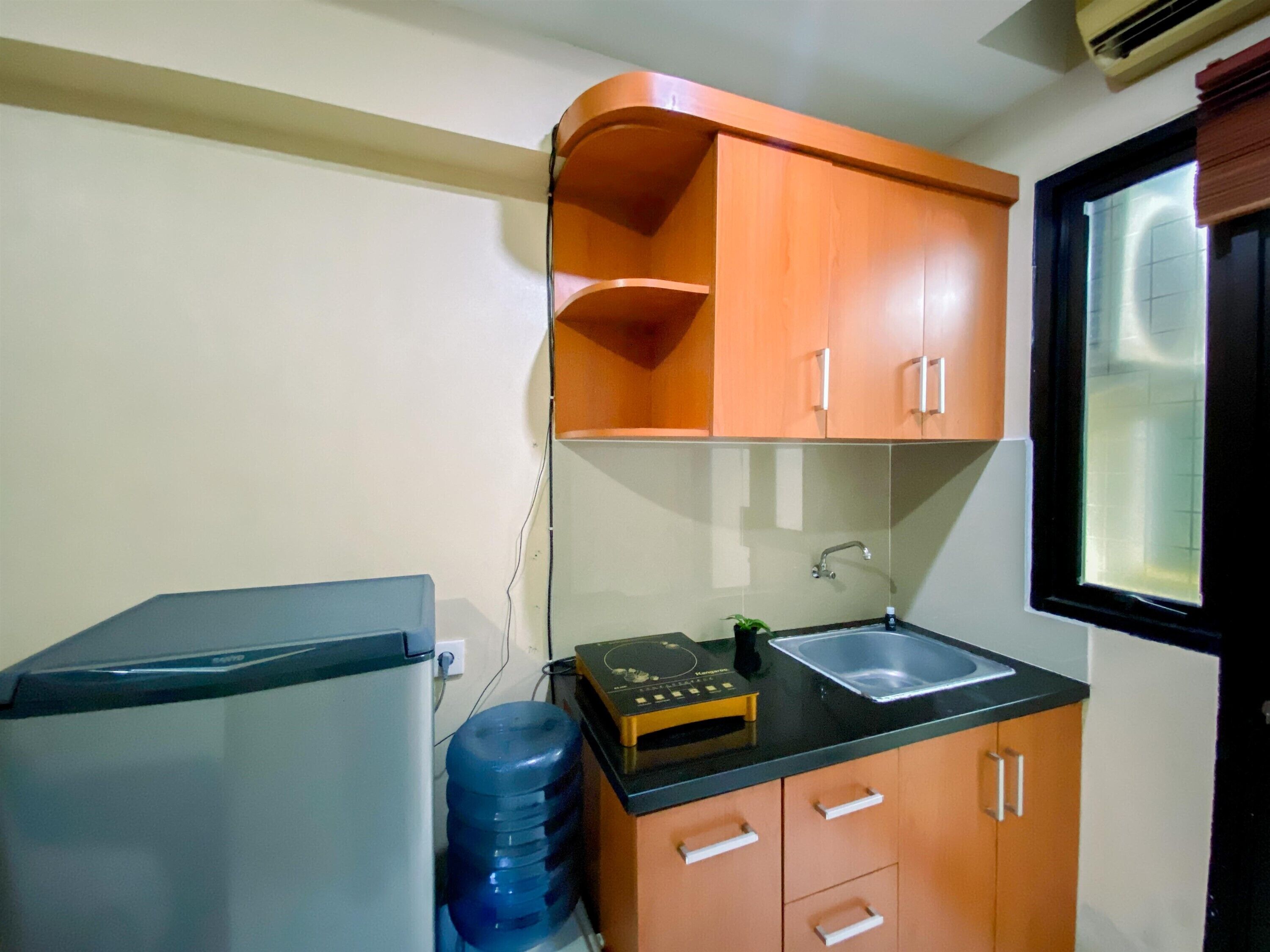 A compact kitchen with a refrigerator, a water dispenser, a sink, and wooden cabinets.