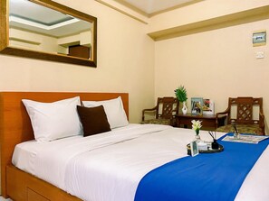 Une chambre d’hôtel avec un lit bien fait, un mur d’accent bleu, une table à manger avec des chaises et un miroir au-dessus du lit.