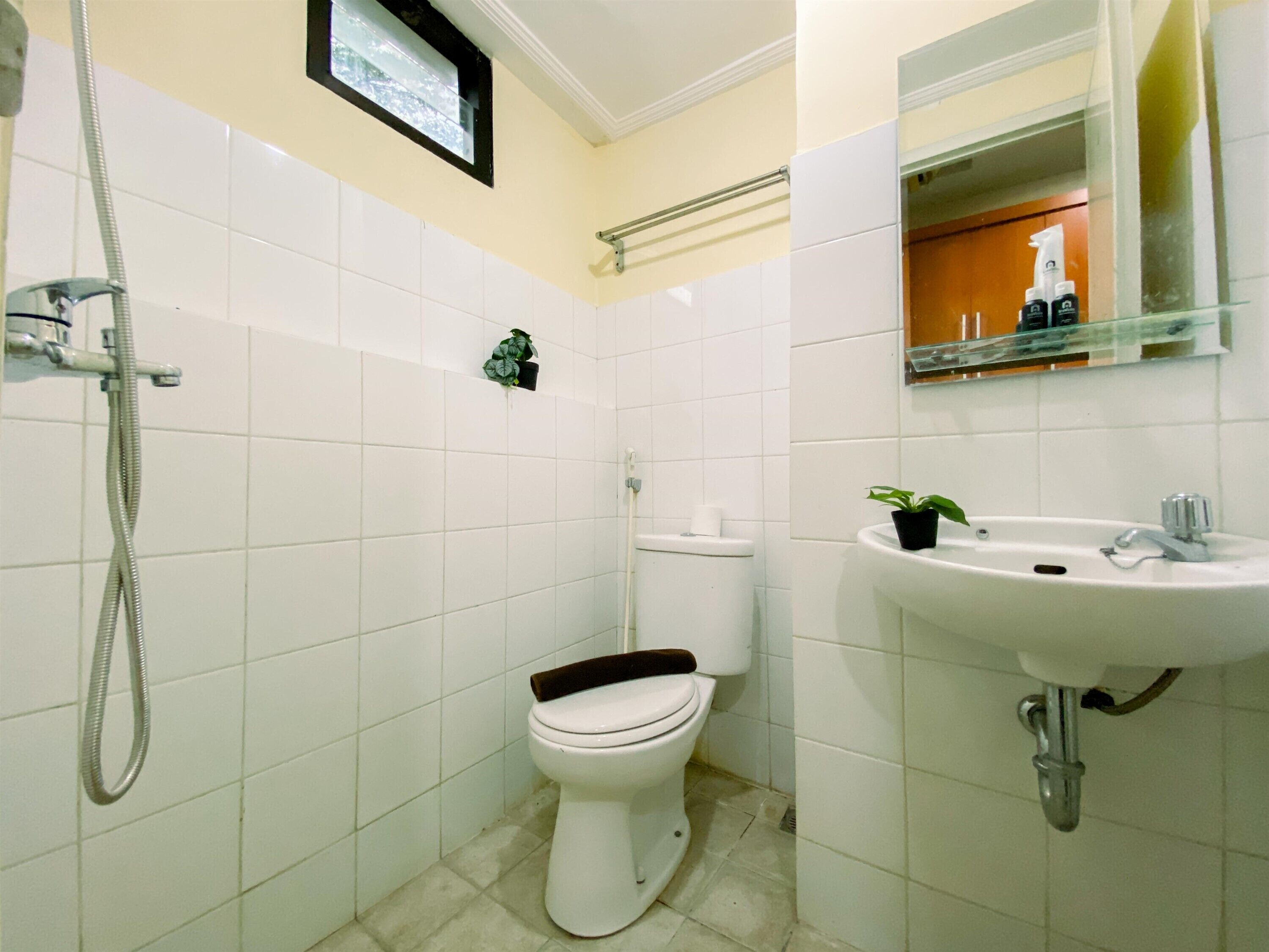 Une salle de bain avec des carreaux blancs, des toilettes, un lavabo et une douche.