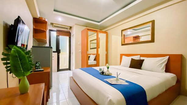 Une chambre d’hôtel avec un lit, un bureau, une télévision et une plante.