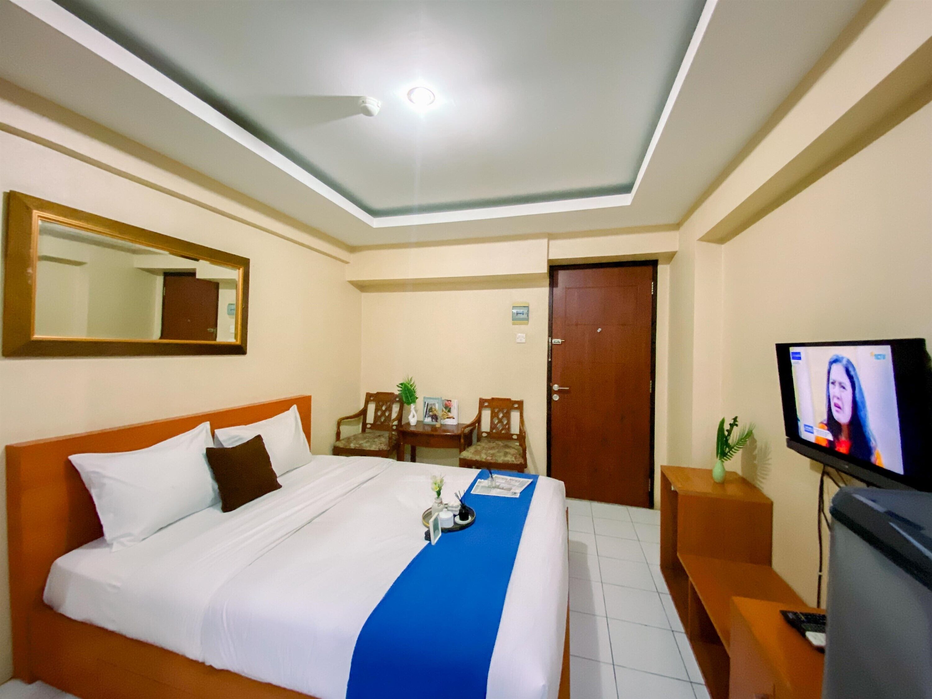 A hotel room with a bed, a desk, a television, and a mirror.