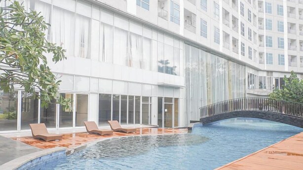 Una piscina con sillas de descanso y un puente de piedra, rodeada por un edificio moderno con ventanales amplios.