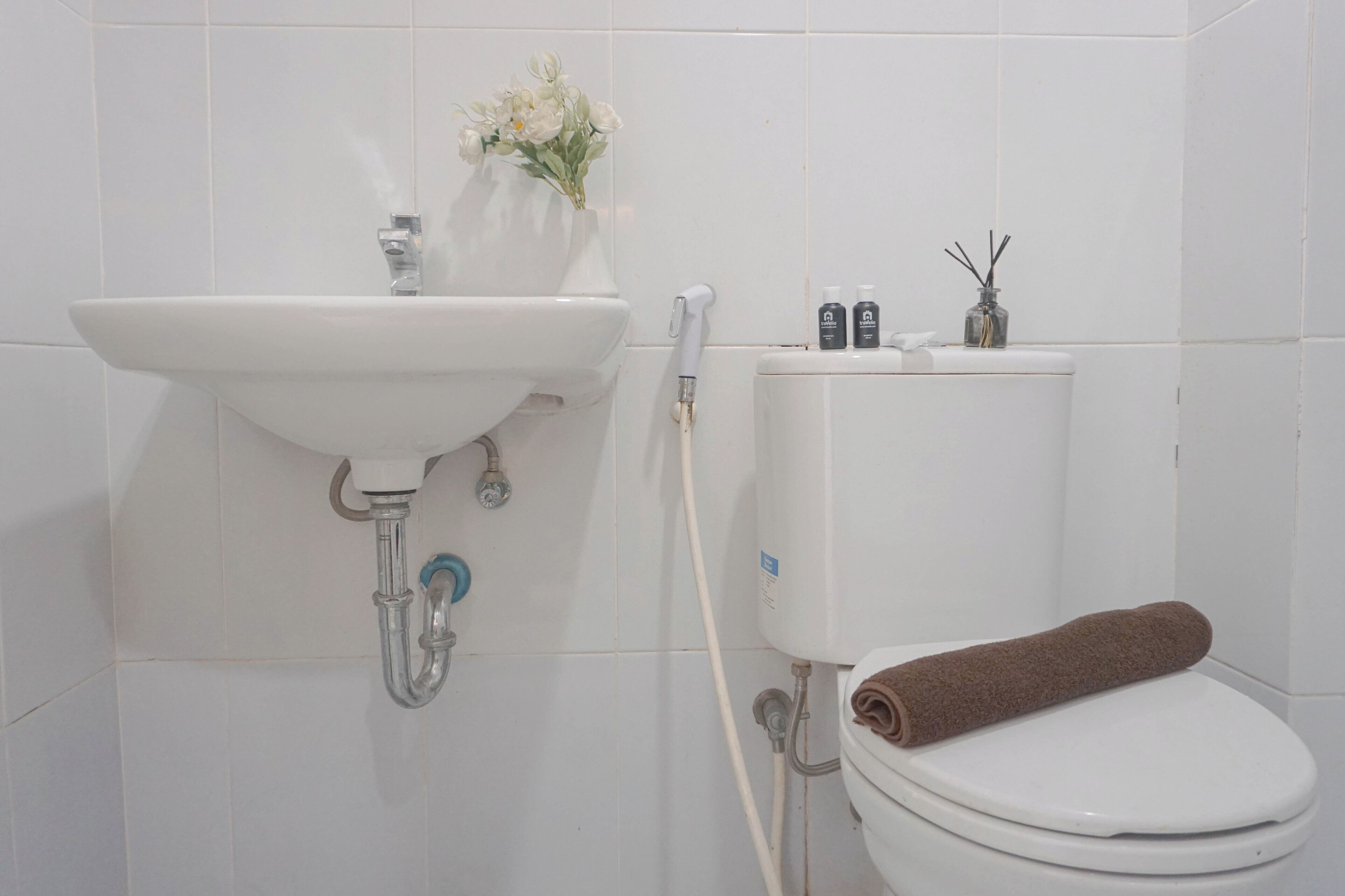 Une salle de bain avec un lavabo blanc, des toilettes et une serviette posée sur la lunette des toilettes.