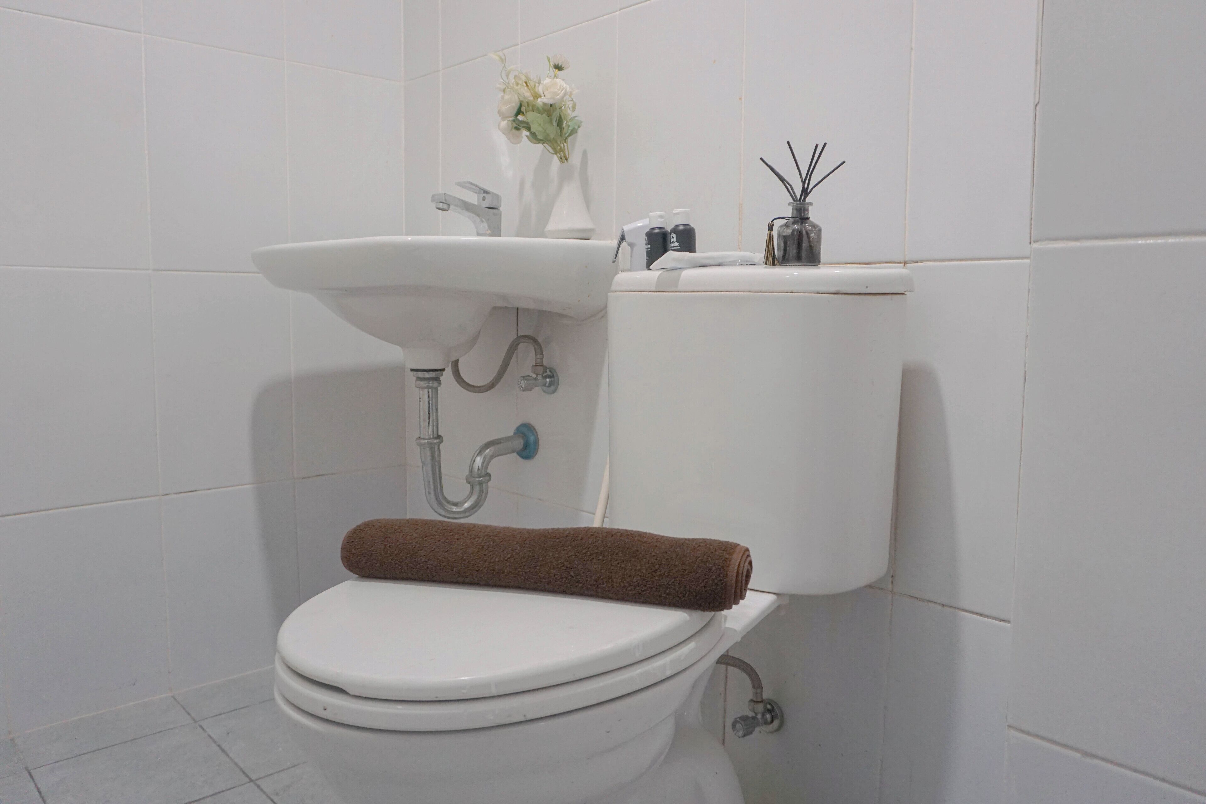 Des toilettes blanches avec une serviette marron posée sur le couvercle, un lavabo blanc et un vase avec des fleurs accroché au mur.