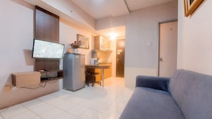 Un espacio habitable compacto con sofá, televisor, dispensador de agua y una pequeña cocina.