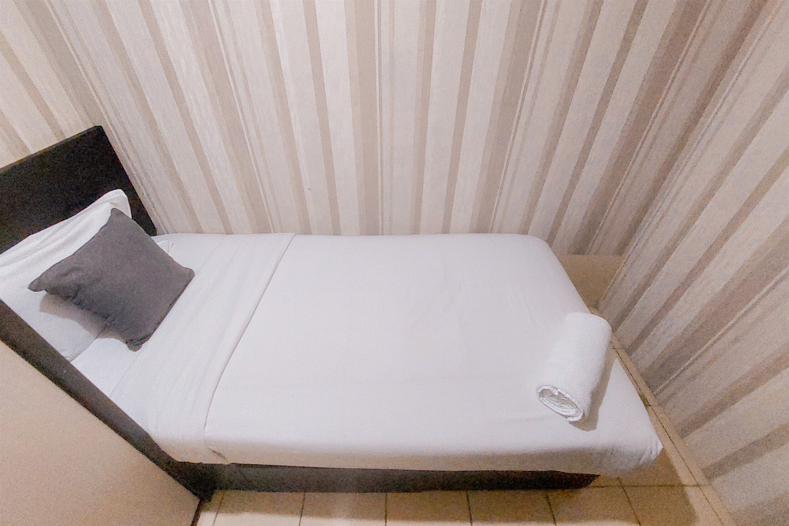 A small, single-bed room with a striped curtain backdrop, a dark headboard, and a neatly made bed with a folded towel.