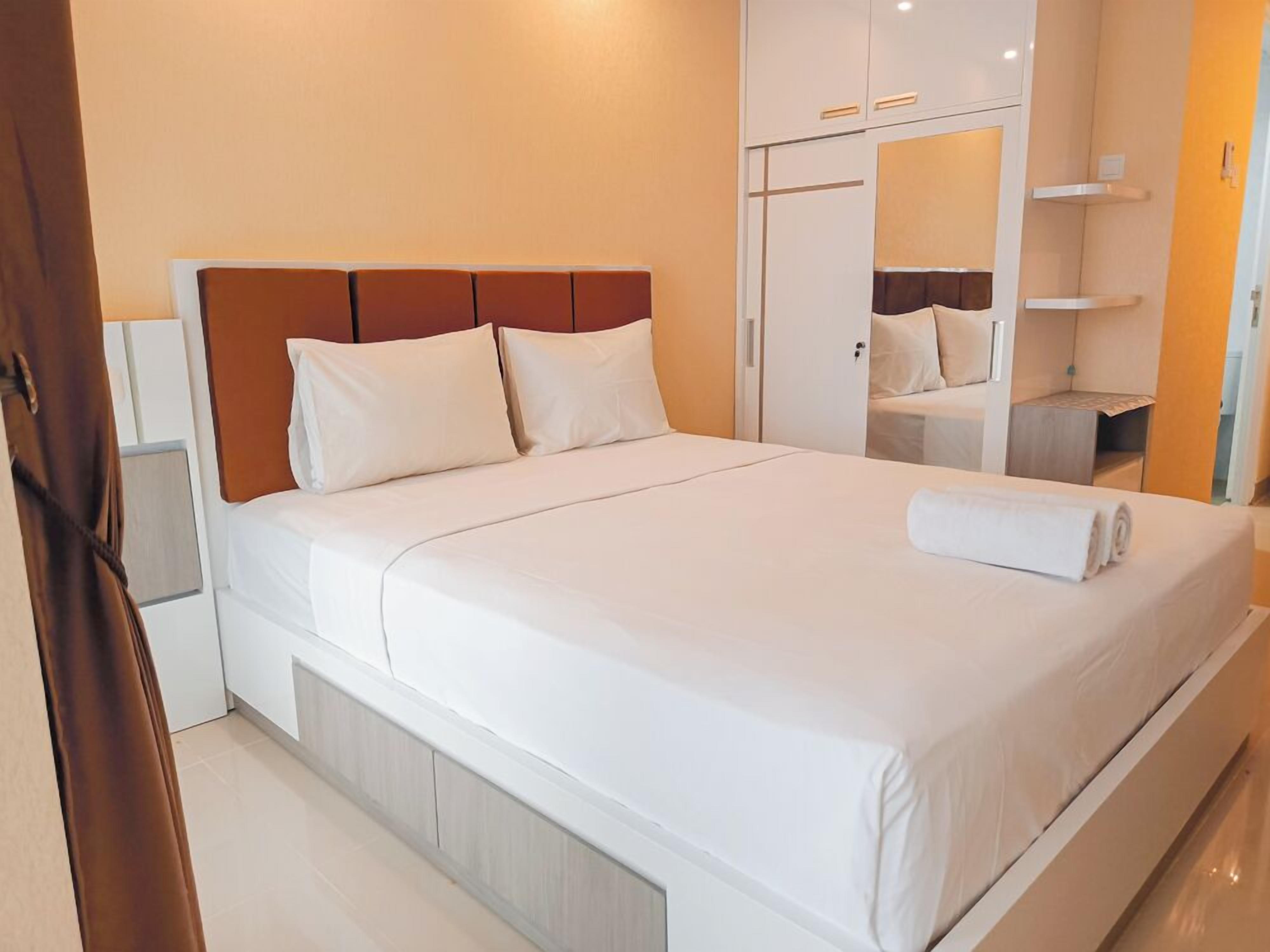 Una cama bien hecha con sábanas y almohadas blancas, un cabecero de madera y un armario blanco con espejo.