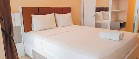 A neatly made bed with white linens and pillows, a wooden headboard, and a white wardrobe with a mirror.