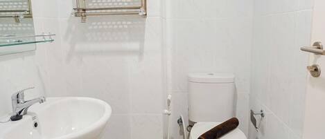 A bathroom with a white sink, a toilet, and a glass shelf above the sink.