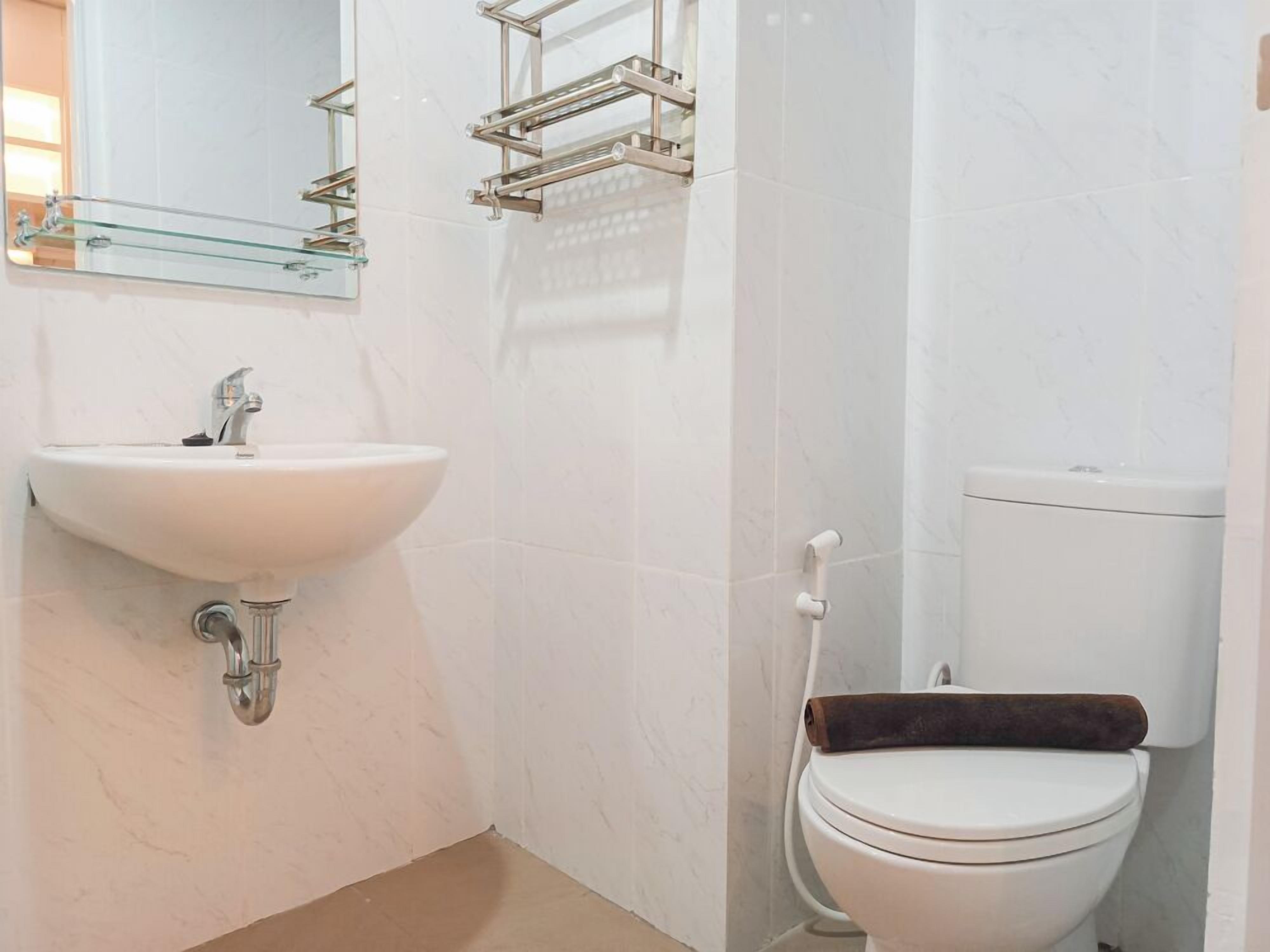 A bathroom with a white sink, a mirror, a glass shelf, and a toilet.