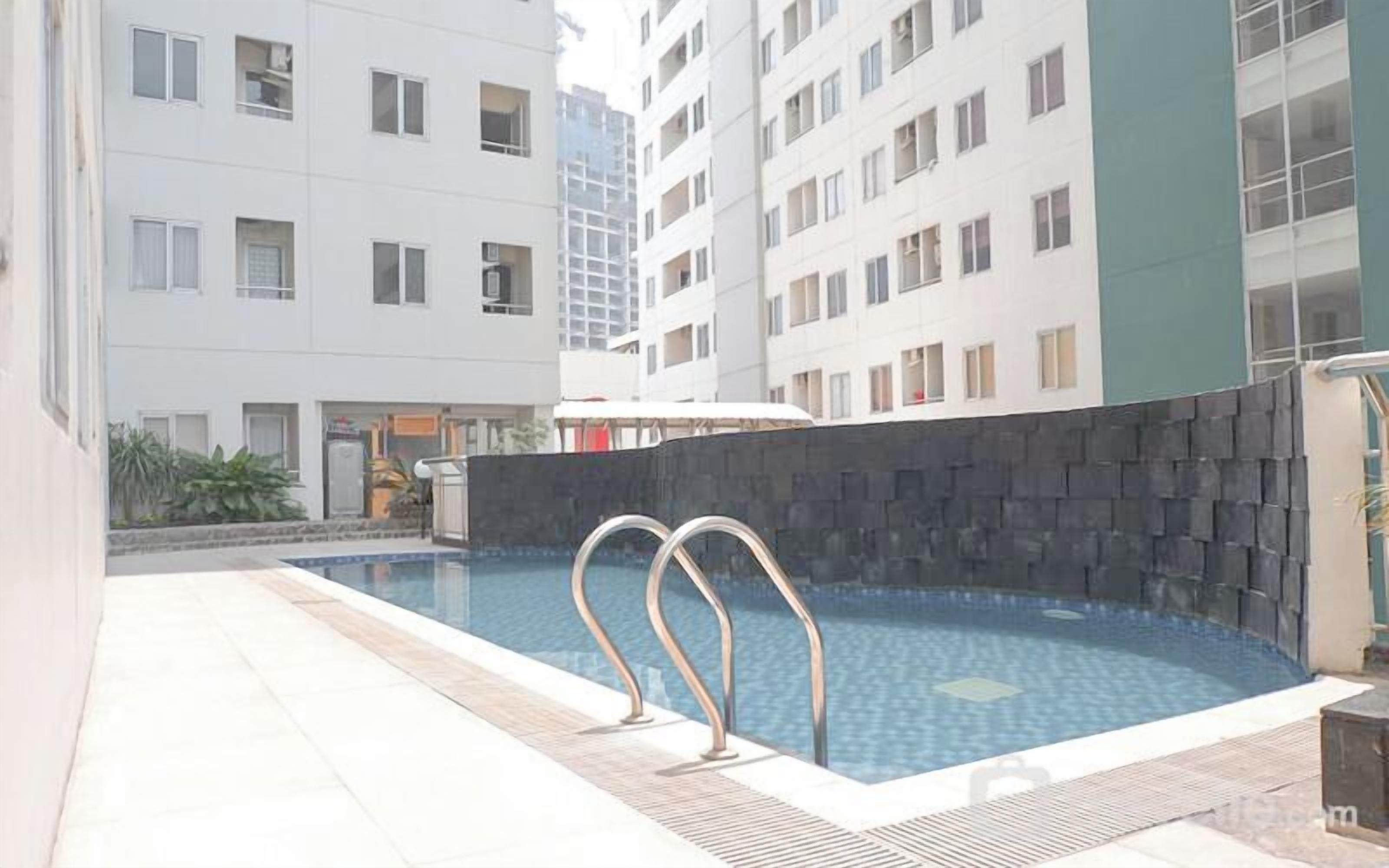 A swimming pool with two metal ladders, surrounded by a tiled deck and a low stone wall.